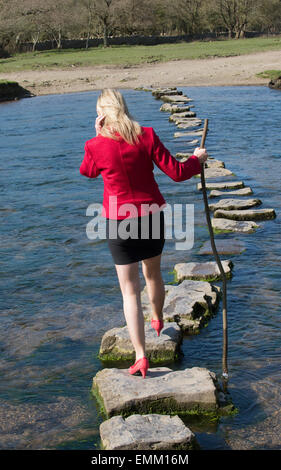 Stepping Stones smartly dressed woman crossing river à l'aide d'une branche d'arbre pour l'équilibre. Balade sur la rivière dans le sud de Ogmore W Banque D'Images