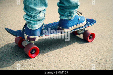 Jeune skateur professionnel en jeans et gumshoes debout sur son skate. Close-up fragment de skateboard et les pieds, photo avec ton rétro Banque D'Images