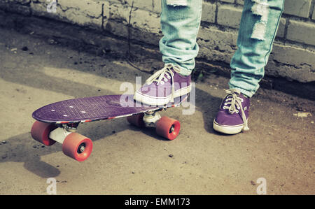 Adolescent pieds de jeans et gumshoes près de skateboard avec mur de brique urbains gris, photo avec retro correction tonale, instagram ancien Banque D'Images