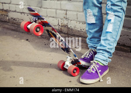 Adolescent pieds en jeans et baskets avec près de skateboard urbain mur gris, photo avec correction tonale rétro, instagram ancien Banque D'Images