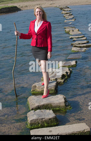 Stepping Stones smartly dressed woman crossing river à l'aide d'une branche d'arbre pour l'équilibre. Balade sur la rivière dans le sud de Ogmore W Banque D'Images