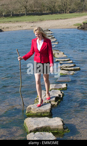 Stepping Stones smartly dressed woman crossing river à l'aide d'une branche d'arbre pour l'équilibre. Balade sur la rivière dans le sud de Ogmore W Banque D'Images