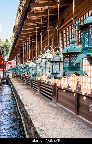 Rangée de lanternes en bronze vert terni suspendues sur terrasse en bois de la salle principale par petit ruisseau au Kasuga Taisha Temple, à Nara. Banque D'Images