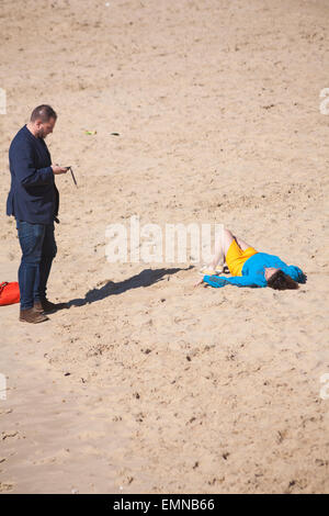 Bournemouth, Dorset, UK. 22 avril, 2015. Homme se tenait à l'aide de téléphone pendant la femme se trouve sur la plage en profitant du soleil sur la plage de Bournemouth en avril. Credit : Carolyn Jenkins/Alamy Live News Banque D'Images