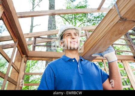 Thoughtful worker carrying wooden planks at site Banque D'Images