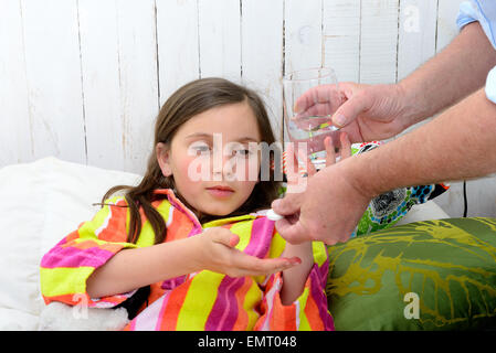 Une petite fille dans le lit en tenant comprimé avec de l'eau Banque D'Images