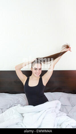 Les cheveux. Belle femme ou fille avec de longs cheveux noirs en bonne santé dans le lit. Heureux les jeunes femmes attrayantes en matinée avec smile holding h Banque D'Images