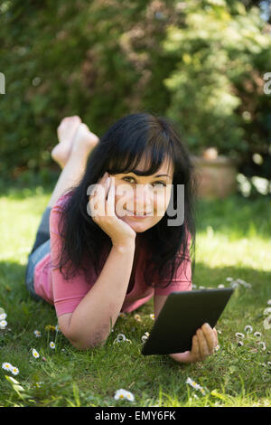 Jeune femme sur l'herbe verte au jardin lecture livre électronique (ebook) Banque D'Images