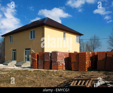 Nouvelle maison jaune avec des piles de briques rouges pour la construction aux beaux jours de printemps Banque D'Images