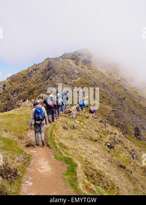 Ramblers walking up Rhyd Ddu chemin sur Bwlch principal avec vue de nuages bas sur le mont Snowdon au sommet du Parc National de Snowdonia au Pays de Galles UK Banque D'Images