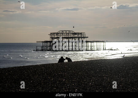 Un couple sur la plage de Brighton, avec le reste de la jetée Ouest détruit dans l'arrière-plan Banque D'Images