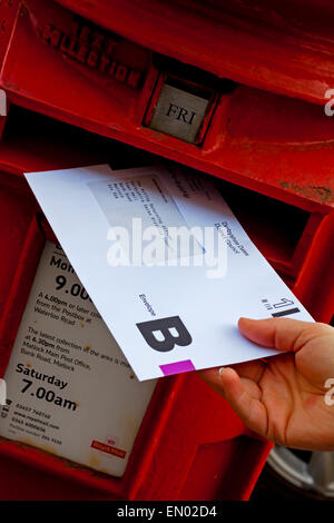 Personne publiant un bulletin de vote postal britannique enveloppe pour une élection dans un style British red pillar box Banque D'Images