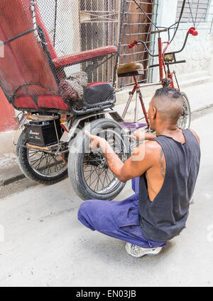 Un homme cubain hispaniques pedicab driver change un pneu à plat sur son 3-roues à La Havane, Cuba. Banque D'Images