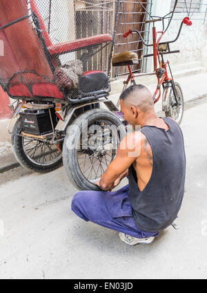 Un homme cubain hispaniques pedicab driver change un pneu à plat sur son 3-roues à La Havane, Cuba. Banque D'Images