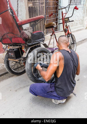 Un homme cubain hispaniques pedicab driver change un pneu à plat sur son 3-roues à La Havane, Cuba. Banque D'Images