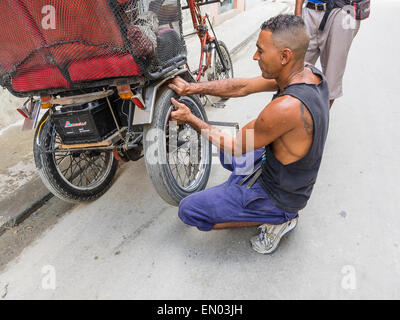 Un homme cubain hispaniques pedicab driver change un pneu à plat sur son 3-roues à La Havane, Cuba. Banque D'Images