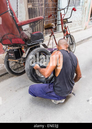 Un homme cubain hispaniques pedicab driver change un pneu à plat sur son 3-roues à La Havane, Cuba. Banque D'Images