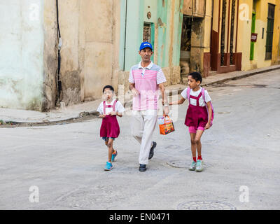 Un père cubain hispaniques promène son deux jeunes filles, qui sont vêtus de l'uniforme scolaire, dans la rue à l'école primaire Banque D'Images