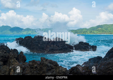 Vagues se briser sur les rochers avec un paradis plage et montagne en arrière-plan Banque D'Images