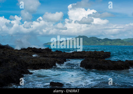 Vagues se briser sur les rochers avec un paradis plage et montagne en arrière-plan Banque D'Images