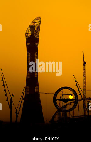 Le soleil se couche derrière l'Aspire tower hotel à Doha, Qatar, avec des grues qui participent à des travaux sur le stade de football de Khalifa sur le r Banque D'Images