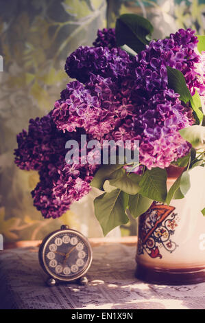 Fleurs lilas dans un pot en céramique avec vintage petit réveil sur surface dentelle blanche Banque D'Images