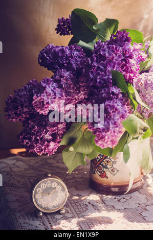 Fleurs lilas dans un pot en céramique avec vintage petit réveil sur surface dentelle blanche Banque D'Images