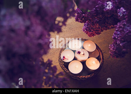 Petites bougies blanches dans un panier entouré par de beaux lilas pourpre. Banque D'Images