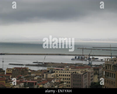 L'horizon de Cagliari avec bâtiments, port, mer et ciel nuageux gris sombre en Sardaigne Banque D'Images