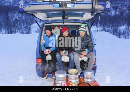 Trois hommes assis à l'arrière d'un camper van cuisiner un repas du soir sur les poêles à l'extérieur en hiver Trangia la neige. Alpes de Lyngen Norvège Banque D'Images