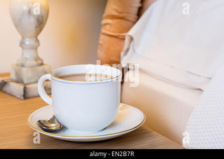 Tasse de thé et soucoupe du matin anglais sur une table de chevet sur le côté d'un lit. Style de vie quotidien. Angleterre Royaume-Uni Grande-Bretagne Banque D'Images