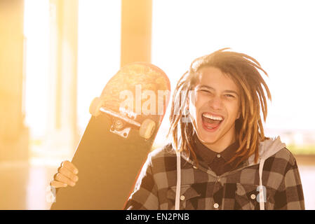 Portrait de jeune homme avec des cheveux rasta et skateboard dans un concept de vie filtre appliqué à chaud Banque D'Images