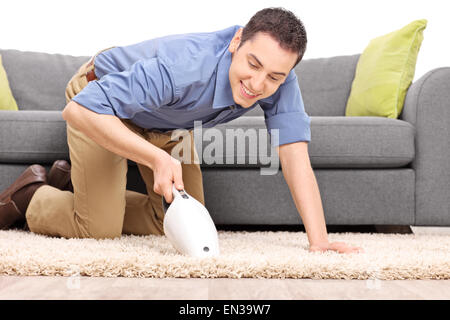 Jeune homme joyeux l'aspirateur sur un tapis avec un aspirateur portable isolé sur fond blanc Banque D'Images