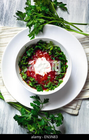 Le bortsch soupe russe au bol blanc servi avec verdure fraîche et bien le persil Banque D'Images