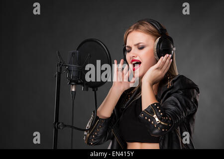 Portrait d'une belle femme singing into microphone avec un casque en studio sur fond noir Banque D'Images
