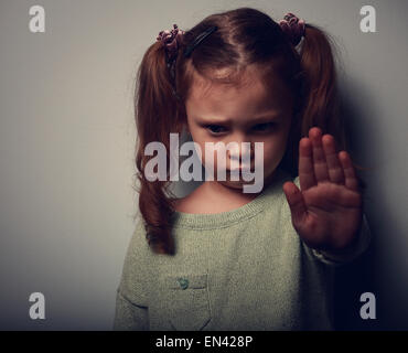 Kid girl montrant la signalisation à main pour arrêter la violence et de la douleur et de regarder sur fond sombre. Closeup portrait couleur Banque D'Images