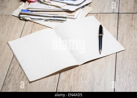 Dans l'image un cahier avec des feuilles blanches et un stylo avec des lettres en arrière-plan. Banque D'Images
