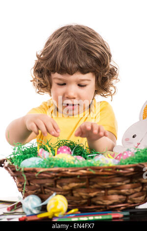 Bébé garçon organiser les oeufs de Pâques dans un panier à l'arrière-plan blanc Banque D'Images