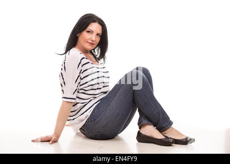 Smiling casual woman sitting on floor against white background Banque D'Images