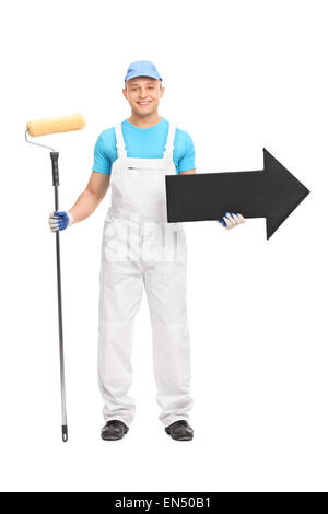 Portrait d'un jeune homme dans un uniforme blanc décorateur tenant un rouleau à peindre et une grande flèche noire pointant vers la droite Banque D'Images