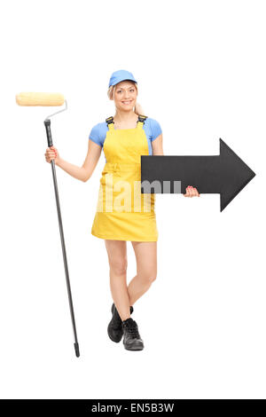 Portrait d'une femme peintre dans un uniforme jaune tenant un rouleau à peindre et une grande flèche noire pointant vers la droite Banque D'Images