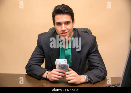 Jeune homme, assis à sa table de travail, compter les espèces en main Banque D'Images