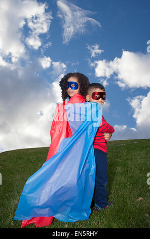 Petit garçon et fille superheros contre le ciel bleu Banque D'Images