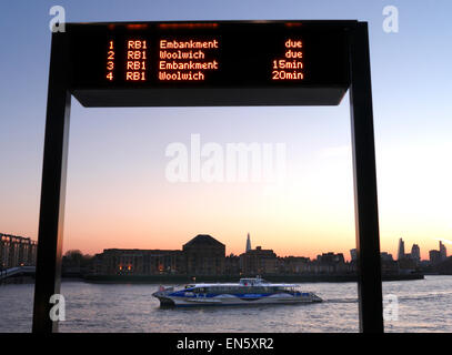 RIVER BOAT & l'écran informations arrivées et RB1 de la rivière Thames Clipper voile au coucher du soleil arrivant à Canary Wharf, à Londres et dans la ville d'échardes b/g E14 Banque D'Images