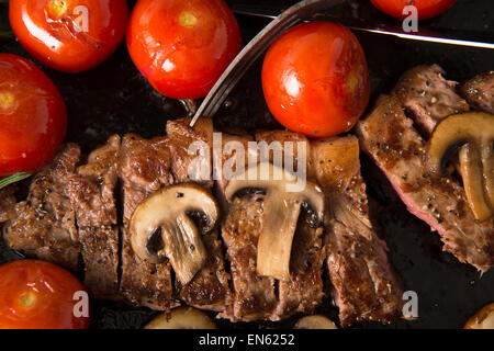 Contre-filet de cuisson dans la poêle en fonte : Steak est cuites et tranchées - illustré avec des tomates grillées et champignons Banque D'Images