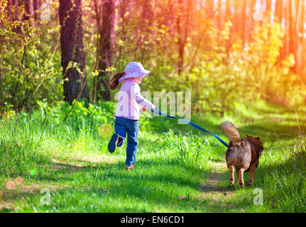 Petite fille avec un chien qui court autour de dans les bois Banque D'Images