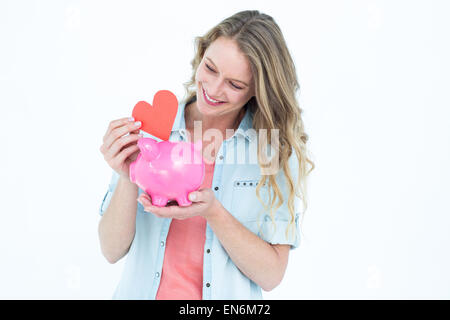 Smiling woman holding piggy bank et coeur rouge Banque D'Images