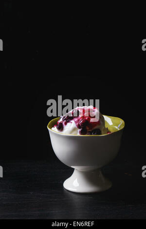 Vase en céramique blanc avec glace vanille, servi avec mélange de fruits rouges sur le tableau noir Banque D'Images