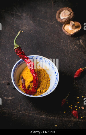 Curcuma en poudre dans un bol en porcelaine, servi avec des champignons shiitake et Red Hot Chili Peppers sur tableau noir. Banque D'Images