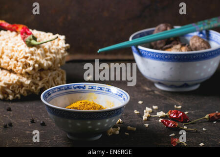 Nouilles sèches pour la soupe de Ramen avec curcuma poudre et les champignons shiitake dans des bols en porcelaine, servi avec Red Hot Chili Peppers sur Banque D'Images